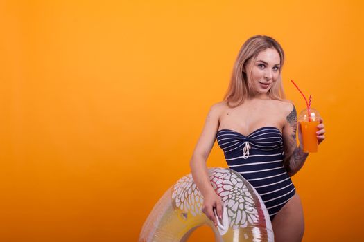 Portrait of love young woman in swimming suit holding a swimming ring over yellow background in studio. Sexy caucasian woman in swimming suit.