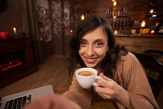 Attractive young woman holding a camera and a cup of coffee taking a selfie. Girl having fun in a coffee shop. Young woman holding a cup of coffee.