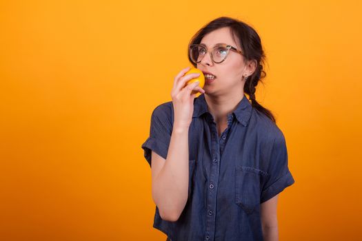 Portrait of cute young woman freaked out with orange in her hand over yellow background in studio. Girl with delicious orange.