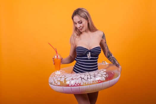 Girl in swimming suit ready for summer vacation over yellow background. Gorgeous young woman with slim body in a swimming ring.