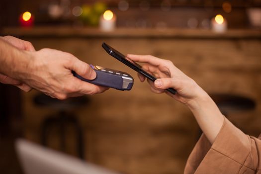 Cropped image of woman paying with mobile phone technology in a coffee shop. Woman using mobile phone. Customer paying barista.