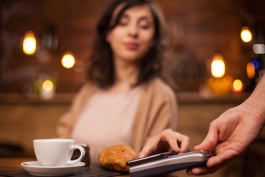 Photo of attractive woman paying with mobile phone using wireless payment on a coffee shop. Beautiful woman using wireless technology to pay coffee in a coffee shop.