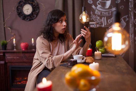 Portrait of shocked young woman sitting at a bar counter in a coffee shop looking at her phone. Hipster young woman using moder mobile phone.