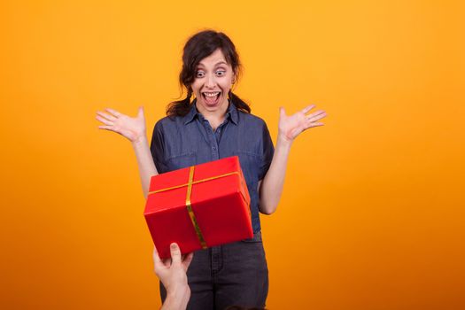 Portrait of amazed beautiful young woman receiving a gift in studio over yellow background. Caucasian beautiful woman shocked.