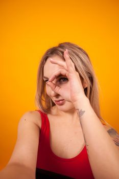 Sexy young woman in red swimming suit making a selfie and showing ok sign over yellow background. Gorgeous young woman in swimming suit.