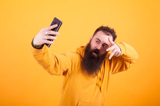 Cool Bearded man wearing yellow hoodie and taking selfie over yellow background. Hipster man. Stylysh man,