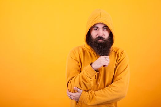 Cool Hipster playing with his long beard and looking at the camera over yellow background. Handsome man. Stylish man. Cool beard.