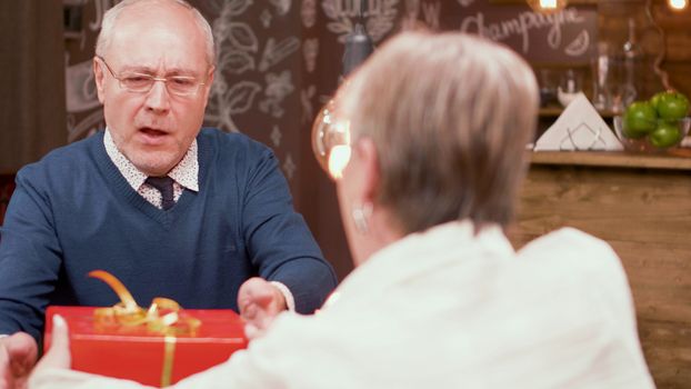 Senior man shocked by the gift that his wife gave him during mealtime in a restaurant. Mature couple.
