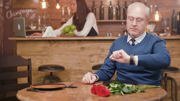 Senior man checking his watch in a restaurant with flower on the table. Relaxed man. Mature man.