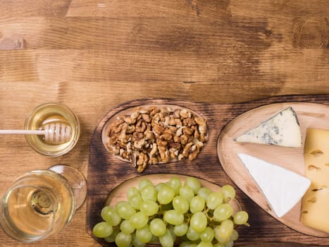 Top view of white wine served with honey on wooden table. French cheese. Tasty grapes. Delicious honey, Copy space available.