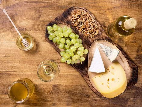 Top view of various cheeses on wooden table in a vintage pub. Fresh grapes. Wine and glass of wine. Tasty wolnuts.