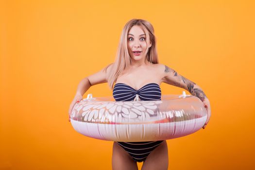 Carefree attractive caucasian woman in swimming suit and swim ring over yellow background. Ready for vacation. Holiday mood.