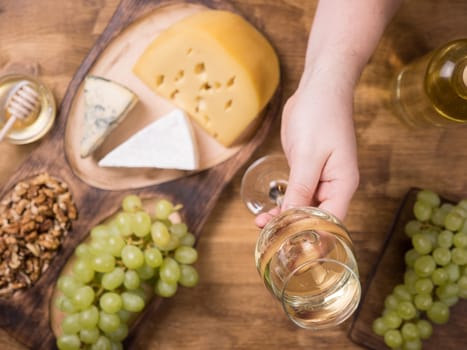 Top view of a glass of wine holded by a man over a wooden table. French cheese. Fresh grapes. Tasty wolnuts.