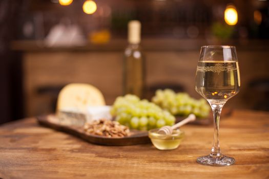 Glass of white wine with super consisting french cheese next to walnuts on rustic wooden table. Food tasting. Fresh grapes.