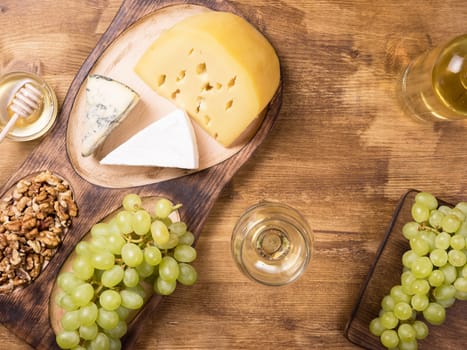 Flat lay top view of various cheeses next to fresh grapes, glass of wine on a wooden table. Copy space available.