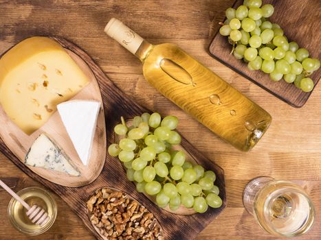 Top view of a bottle of white wine next to fresh grapes on wooden table. Various cheeses. French cuisine.
