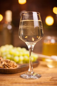Close up photo of a glass of white wine on a wooden table. Delicious grapes. Tasty walnuts.