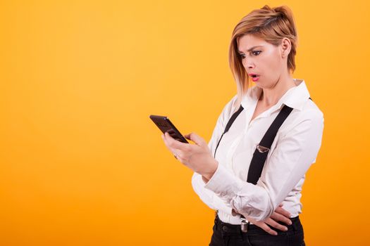 Beautiful woman in white t-shirt looking shocked at the phone over yellow background. Pretty woman. Casual clothes.