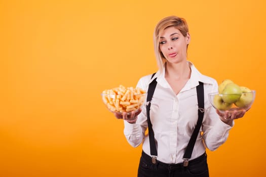 Pretty young woman looking at those delicious corn puffs over yellow background. Delicious green apples.