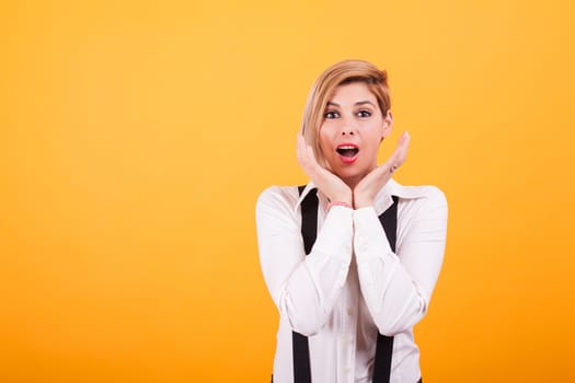 Attractive woman with blond hair looking shocked at camera over yellow background. Beautiful eyes. Facial expression.