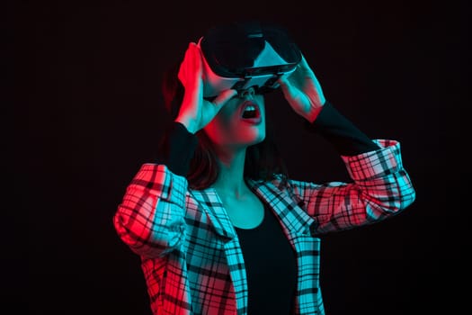 Side view portrait of pretty teenage girl wearing virtual reallity glasses with cyan and red color gels in studio over black background. Teenage girl using modern techonlogy. Cheerful young lady using vr headset.