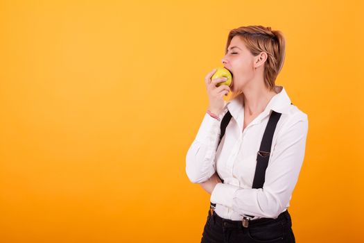Pretty woman with casual clothes taking a big bite from a green apple over yellow background. Beautiful woman eating a green apple.