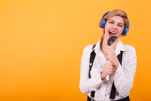 Attractive young woman singing on a black spoon with headphones on her head over yellow background. Cute woman. Modern woman.