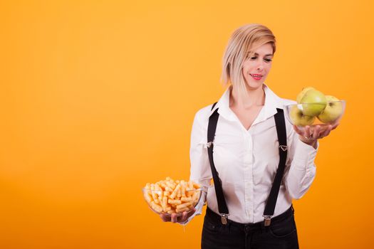 Pretty blonde woman with short hair looking at her bowl of green apples over yellow background. Healthy fruits. Natural food.