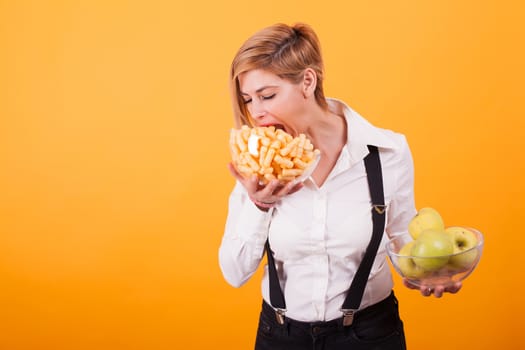 Pretty blond woman with short hair taking a bite from her corn puffs over yellow background. Tasty corn puffs,. Fresh apples. Green apples.