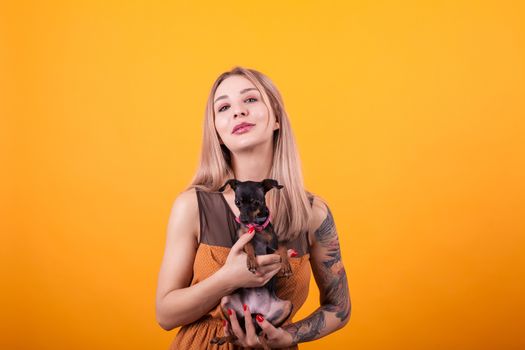Beautiful women with casual dress and her adorable puppy over ellow background. Dog lover. Happy dog owner.