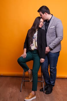 Husband kissing his wife forehead over yellow background. Happy couple. Showing affection.