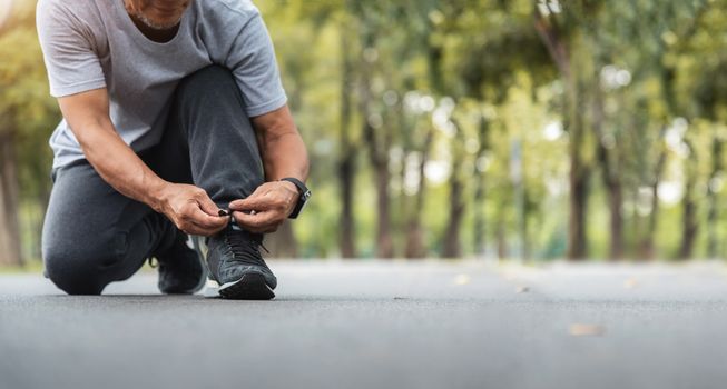 Asian Senior man tying running shoes at the park. Banner, Panoramic.