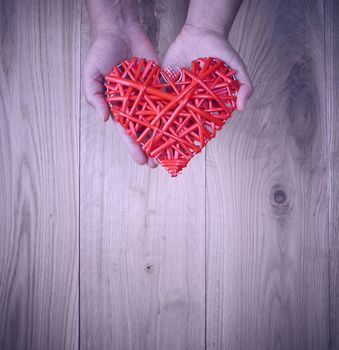 red heart in human hand on yellow wooden background of oak planks