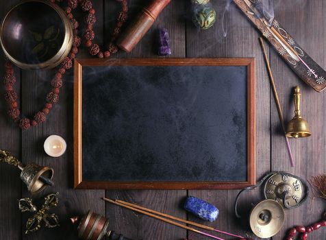 Tibetan singing bowl and other religious ritual instruments for meditation and empty frame on a brown wooden background, top view, 