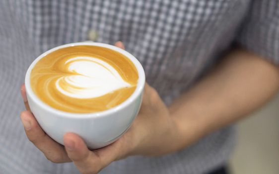 Woman barista holding latte art coffee with heart shape in white cup, selective and soft focus