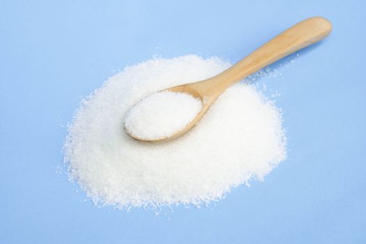 Monosodium glutamate in wood spoon on light blue background, food ingredient