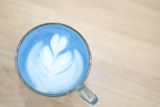 Closeup top view glass of blue milk with latte art tulip shape on wood table, selective focus