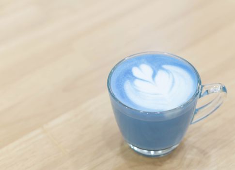 Closeup glass of blue milk with latte art tulip shape on wood table, selective focus