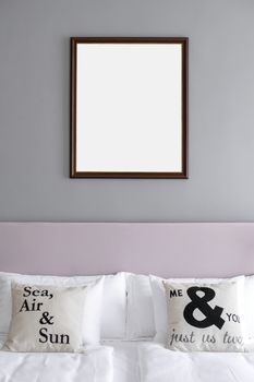 Picture frame mockup hanging on the wall above the bed in a grey and rose theme minimalist bedroom.