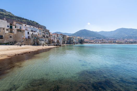 Idyllic view of turquoise sea and houses with Rocca di Cefalu rocky mountain in the background seen from historical old harbour of Cefalu - Sicily, Italy