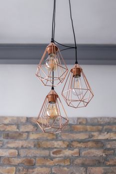 Set of three rose gold light fixtures in front of a white and brick wall background.