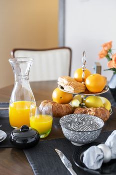 Close shot of continental style breakfast with freshly baked puff pastry and squeezed orange juice served on a dark hardwood dining table.