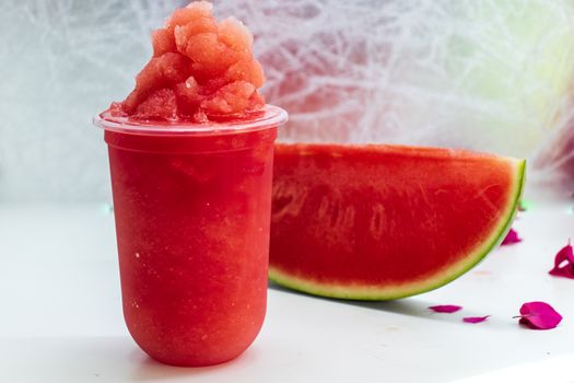 a glass of smoothie watermelon and a piece of watermelon on table