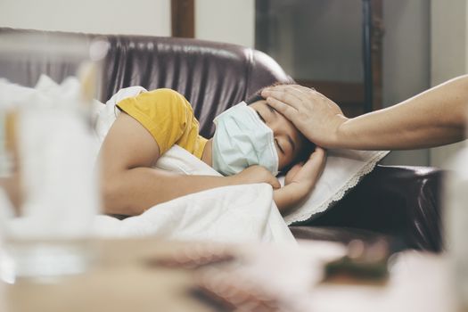 Sick child lying in sofa bed with protection mask on face against infection.