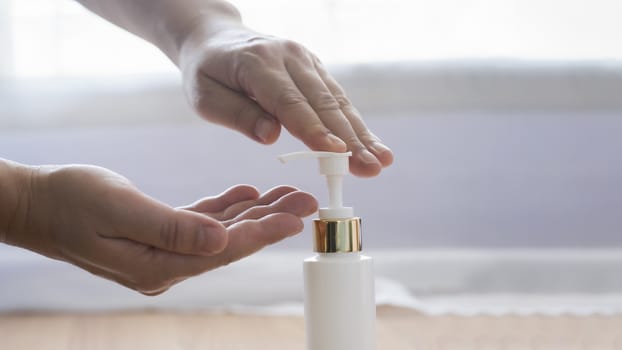 COVID-19, Close up man using bottle of antibacterial wash hand sanitizer gel dispenser, against Novel coronavirus (2019-nCoV) at home.  Home isolation and Healthcare concept.