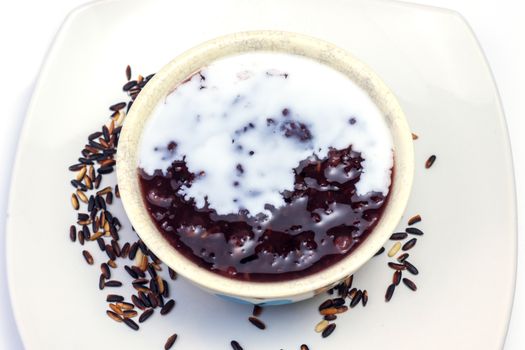 thai black sticky rice wiht sweet coconut milk on top in white plate