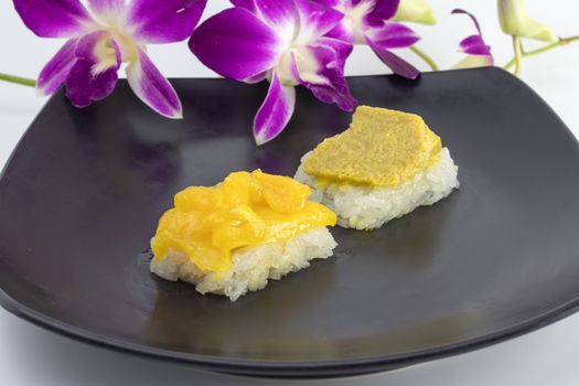 sweet sticky rice topped with egg custard and jackfruit in syrup in black plate decorated in purple orchid