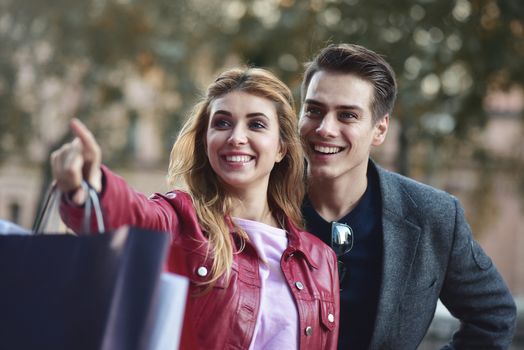 Beautiful couple with shopping bags is talking and smiling while doing shopping in the mall focus on the woman