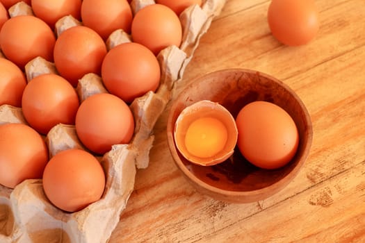 Cracked egg in bowl and egg shells on wooden table.