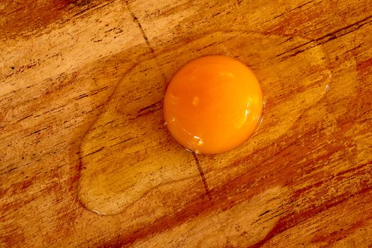 Broken raw egg on the chopping board. Broken egg on brown wooden table. Top view.